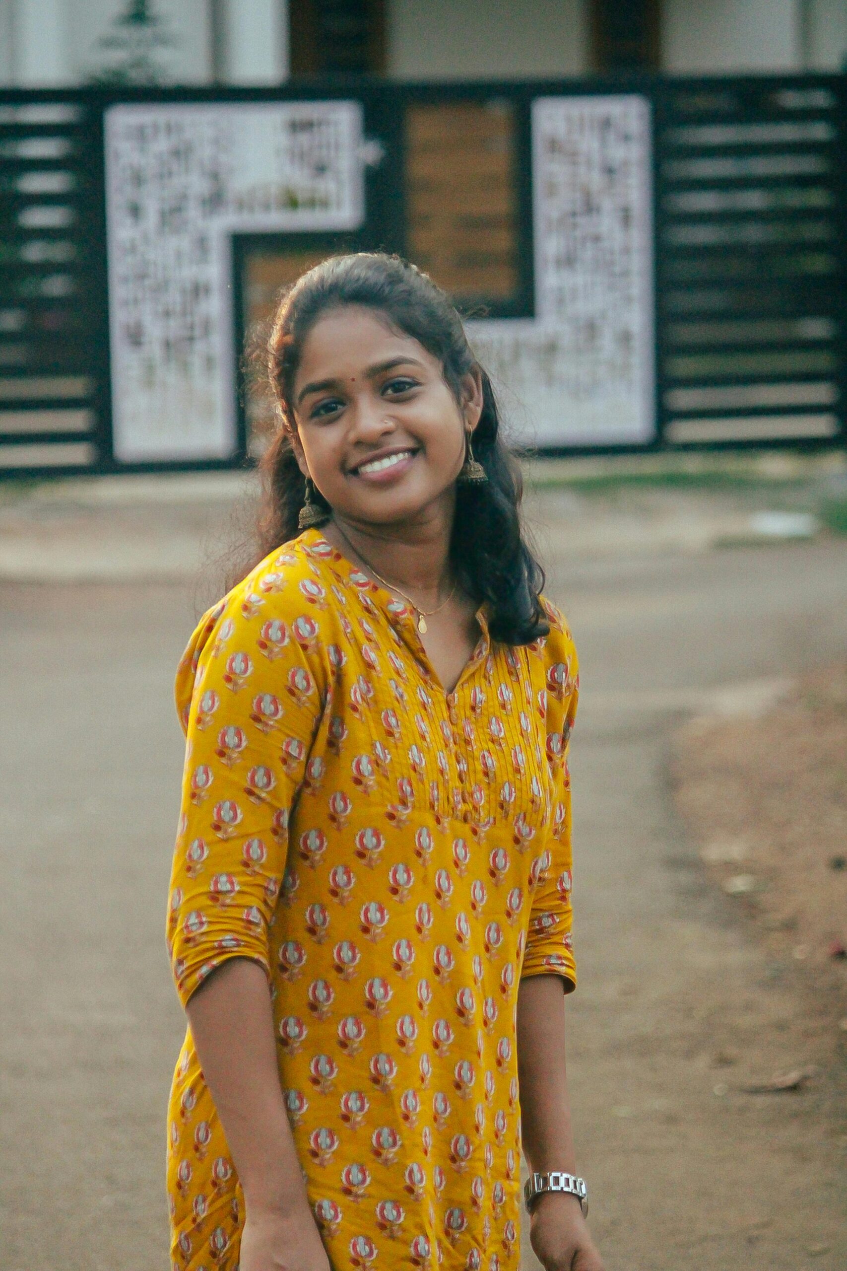 A cheerful young woman in a vibrant yellow dress enjoying an outdoor setting in Kozhikode, India.